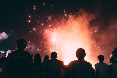 Rear view of people enjoying firework display at night