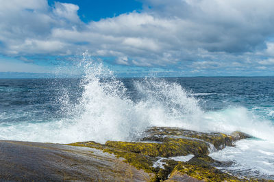 Sea waves splashing on rocks against sky