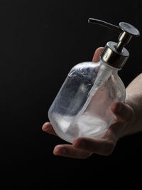 Close-up of hand holding bottle against black background