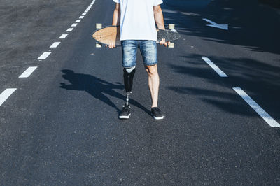 Young man with leg prosthesis holding skateboard on a road
