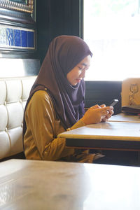 Young woman wearing hijab while using mobile phone at restaurant