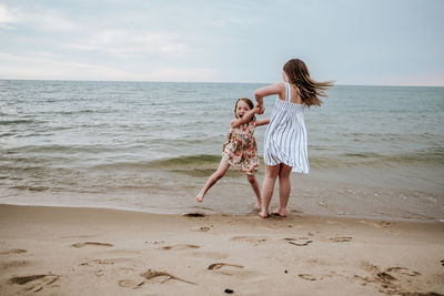 Sisters dancing and playing on beach at lake michigan