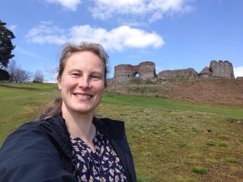 Portrait of smiling woman standing on field against old ruins