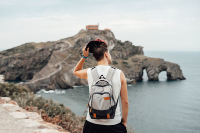 Rear view of man standing on rock by sea against sky