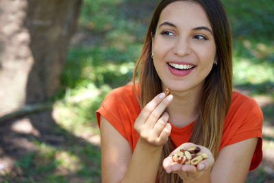 Close-up of beautiful healthy woman eating brazil nuts outoor. looks to the side.