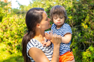 Mother holding son while standing against tree