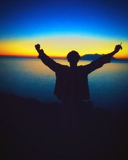 Silhouette man with arms raised in sea at sunset