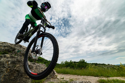 Rear view of man riding bicycle on field against sky