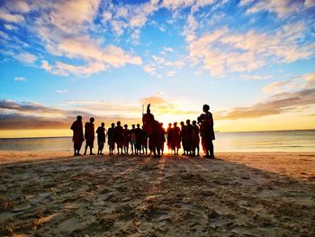 Silhouette people on beach against sky during sunset