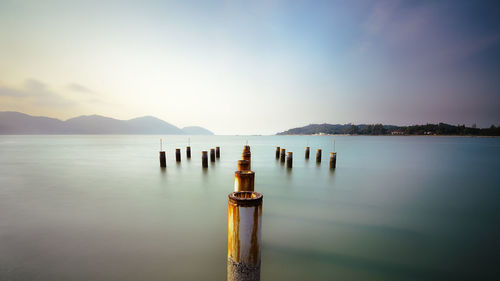 Wooden posts in lake against sky