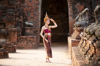 Young woman in traditional clothing standing against built structure