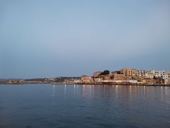 Sea by buildings against clear sky