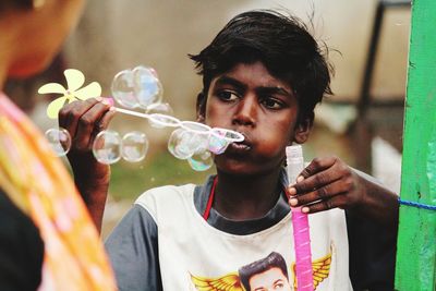 Teenage boy looking away while blowing bubbles outdoors