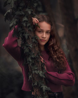 Portrait of young woman standing against tree