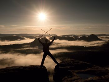 Silhouette person standing on rock against sky during sunset