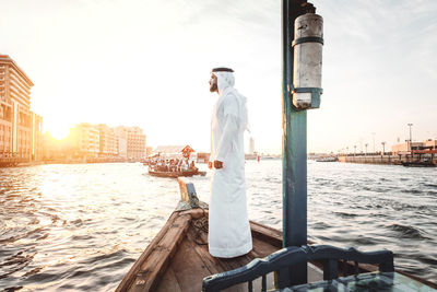 Side view of man standing in boat on river at sunset