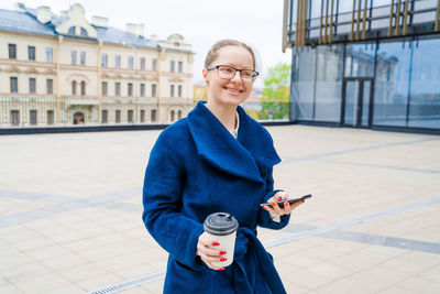 Business woman with phone near office. portrait smiling girl in blue coat