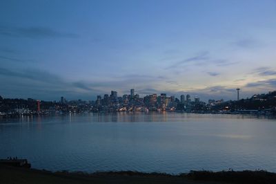 Illuminated city by river against sky at sunset