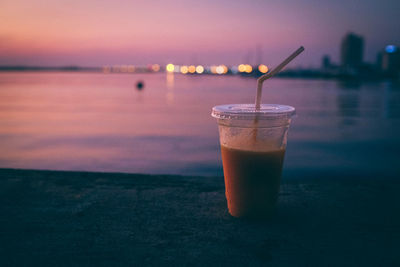 Close-up of drink against sea during sunset