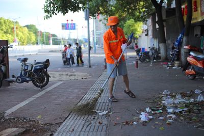 Full length of worker sweeping footpath