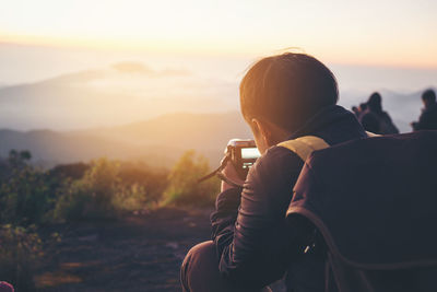 Rear view of man photographing against sky during sunset