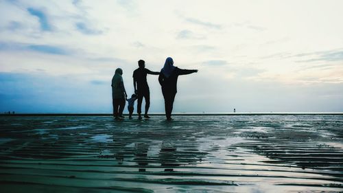 Silhouette people standing by sea against sky