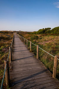 Boardwalk leading towards landscape against clear sky
