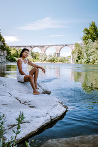 Young woman sitting on bridge against sky