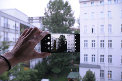 Midsection of man photographing with mobile phone against buildings