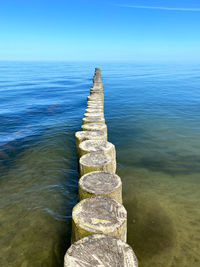 Wooden posts in sea against blue sky