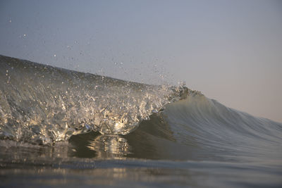 Sea waves splashing on shore against clear sky