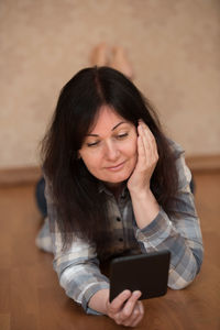 Mature woman using mobile phone while lying on hardwood floor at home