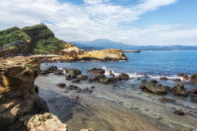 Rocks on shore by sea against sky