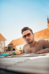Young man in sunglasses resting on edge of swimming pool