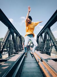 Full length of woman jumping on railway bridge against sky