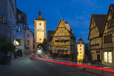 Illuminated street by buildings in city