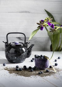 Still life with a black ceramic teapot and a tea cup with blueberries on a light background 