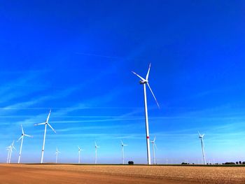 Wind turbines on field against blue sky