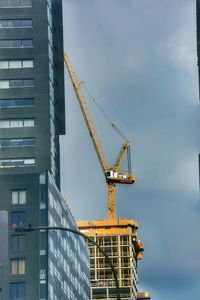 Low angle view of crane by building against sky