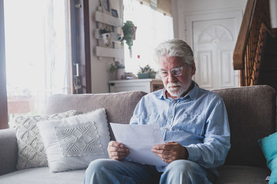 Senior man reading document while sitting on sofa at home