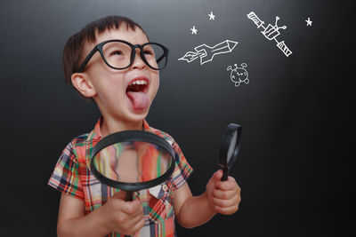 Boy screaming while holding magnifying glasses against blackboard