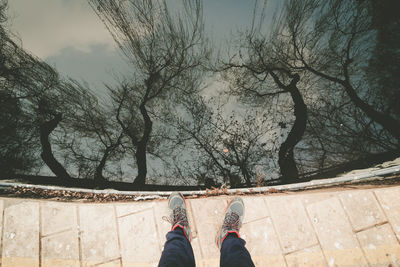 Low section of man standing by lake with trees reflecting