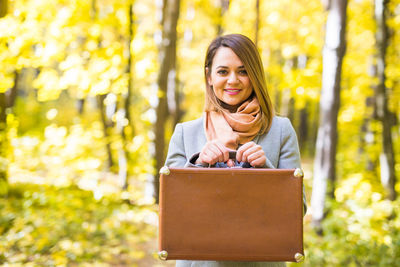 Young woman smiling while standing against trees during autumn