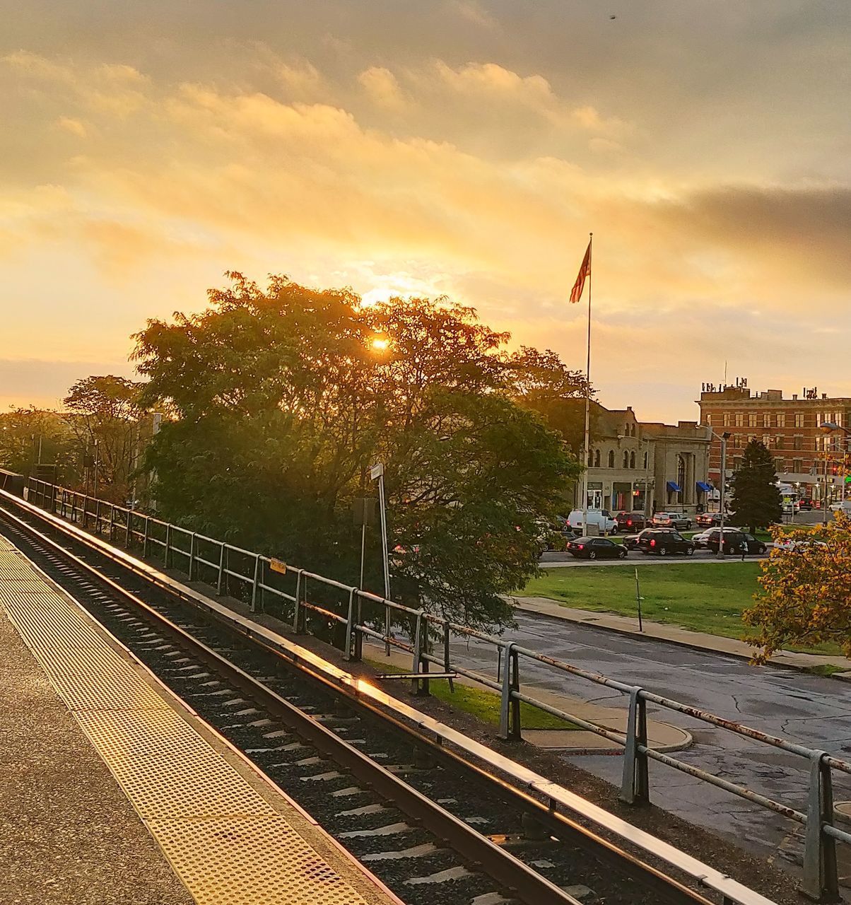 RAILROAD TRACKS BY BUILDINGS IN CITY AGAINST SKY DURING SUNSET