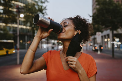 Smiling businesswoman drinking coffee in city during covid-19