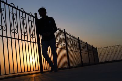 Silhouette man standing by railing against clear sky