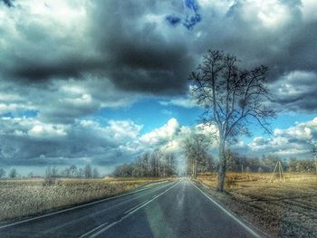 Road passing through field against cloudy sky