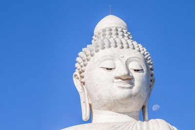 Low angle view of giant buddha statue against clear blue sky