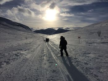 Rear view of man walking on snow covered field against cloudy sky