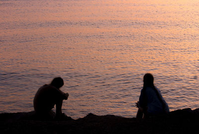 Rear view of couple sitting on land against sky during sunset